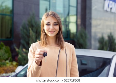 Closeup Portrait Happy, Smiling, Young Attractive Woman, Buyer Near Her New Car Showing Keys Isolated Outside Dealer, Dealership Lot Office. Personal Transportation, Auto Purchase Concept