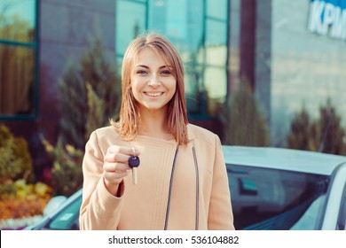 Closeup Portrait Happy, Smiling, Young Attractive Woman, Buyer Near Her New Car Showing Keys Isolated Outside Dealer, Dealership Lot Office. Personal Transportation, Auto Purchase Concept