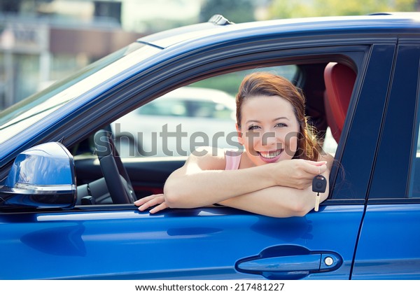 Closeup portrait happy, smiling, young attractive\
woman, buyer sitting in her new blue car showing keys isolated\
outside dealer, dealership lot, office. Personal transportation,\
auto purchase concept
