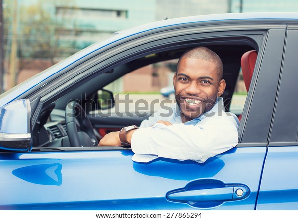 Closeup portrait happy smiling young man buyer\
sitting in his new car excited ready for trip isolated outside\
dealer dealership lot office. Personal transportation auto purchase\
concept