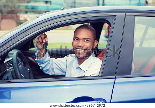 Closeup portrait\
happy, smiling, young man, buyer sitting in his new blue car\
showing keys isolated outside dealer, dealership lot. Personal\
transportation, auto purchase\
concept