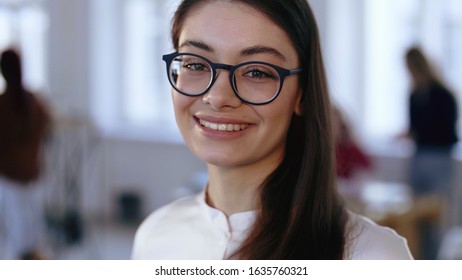 Close-up Portrait, Happy Young Brunette Design Professional Business Woman In Eyeglasses Smiling At Camera At Office.