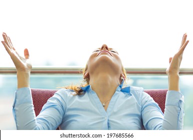 Closeup Portrait Happy Young Business Woman In Blue Shirt Looking Upwards, Hands Raised In Air Relaxing On Black Couch, Isolated City Background. Corporate Life Style. Stress Relief Techniques