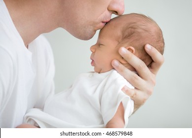 Close-up portrait of happy young father hugging and kissing his sweet adorable newborn child. Indoors shot, concept image - Powered by Shutterstock