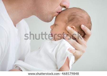 Close-up portrait of happy young father hugging and kissing his sweet adorable newborn child. Indoors shot, concept image
