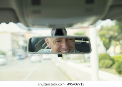 Closeup Portrait, Happy Young Man Driver Looking At Rear View Mirror Smiling, Isolated Interior Car Windshield Background. Positive Human Expression Body Language