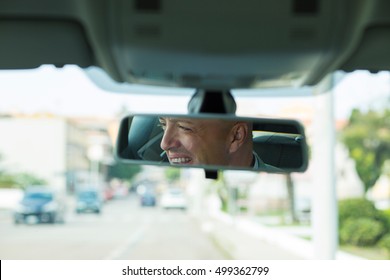 Closeup Portrait, Happy Young Man Driver Looking At Rear View Mirror Smiling, Isolated Interior Car Windshield Background. Positive Human Expression Body Language