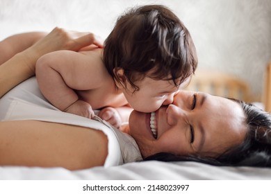 Closeup Portrait Of Happy Young Mother And Infant Girl Lying On Bed In Room. Carefully Hold Naked Baby In Arms On Chest. Selective Focus, Free Copy Space. Concept Of Maternal Affection And Childcare.