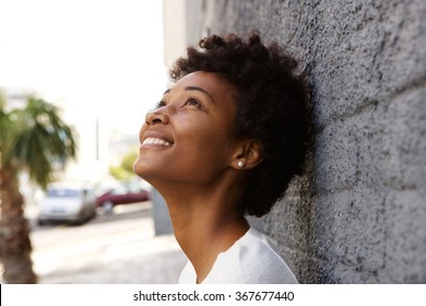 Closeup portrait of happy young woman leaning to a wall and looking up
