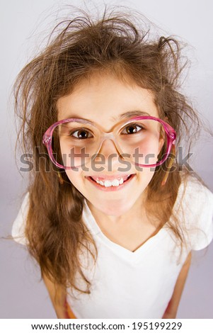 Closeup portrait, headshot happy, smiling , excited, funny looking, little girl with big glasses, messy hair, isolated grey background. Positive human emotions, facial expressions, attitude, reaction