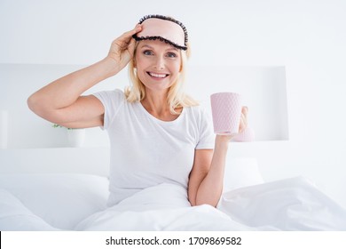 Close-up portrait of her nice-looking attractive shine pretty cheerful cheery glad senior woman drinking warm milk sitting in bed spending weekend in light white interior room flat apartment indoors - Powered by Shutterstock