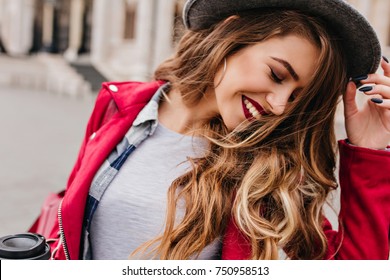 Close-up portrait of inspired caucasian lady with trendy make-up spending vacation in Europe. Outdoor photo of smiling shy girl with light-brown hair walking around city in morning.