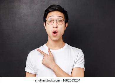 Close-up portrait of interested and surprised, excited young asian guy hear about interesting event going nearby, discuss advertisement with a friend, pointing left and fold lips say wow