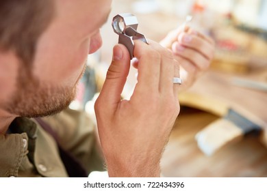 Closeup portrait of jeweler inspecting ring through magnifying glass in workshop