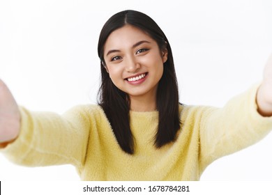 Close-up Portrait Of Kawaii Tender Young Asian Girl Taking Selfie, Apply Photo Filters, Holding Camera Both Hands Sideways And Smiling While Video Call Friend With Mobile Phone, White Background