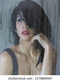 Close-Up Portrait Of Latin Brunette Woman Seen Through Wet Window In A Rainy Day. Sensual Girl With Black Hair And Provocative Look