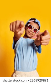 Closeup portrait of little african happy boy in stylish sunglasses and cap looking at camera over bright yellow background. Concept of music, happiness, kids emotions and ad