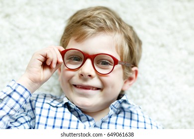 Close-up portrait of little blond kid boy with brown eyeglasses on white background. Happy smiling child in casual clothes. Childhood, vision, eyewear, optician store. Boy choosing new glasses
