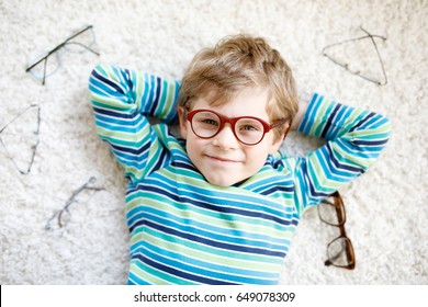 Close-up portrait of little blond kid boy with different eyeglasses on white background. Happy smiling child in casual clothes. Childhood, vision, eyewear, optician store. Boy choosing new glasses