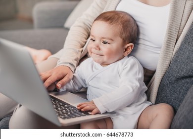 Closeup portrait of little boy with funny facial expression sitting on mother's knees and exploring laptop 
