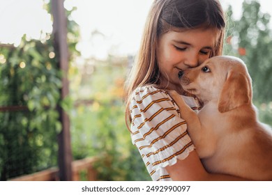 Close-up portrait of a little girl hugging a puppy. A cute small kid is playing with a dog. A sweet child is happy with her pet. A lovely preschool girl takes care of the labrador - Powered by Shutterstock