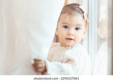 Close-up portrait of a little, one year old baby girl looking behind the curtain
