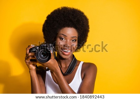 Close-up portrait of lovely cheery wavy-haired brunette girl holding in hands using digicam shooting isolated over bright yellow color background