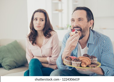 Close-up Portrait Of Lovely Handsome Stylish Cheerful Bearded Guy In Checkered Shirt Eating Many Sweets Lady Sitting On Couch Divan Sofa In Modern Light Apartments