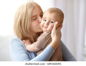 Closeup Portrait Of Loving Mother Young Blonde Woman Kissing Little Kid, Home Interior. Beautiful Lady Bonding With Her Adorable Baby, Holding Cute Sun Or Daughter And Kissing