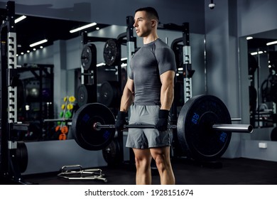 A close-up portrait of a male athlete in a grey fitness t-shirt and shorts. He focused his mind on the best lifting ever in the indoor sports center. Power of the body, physical strong