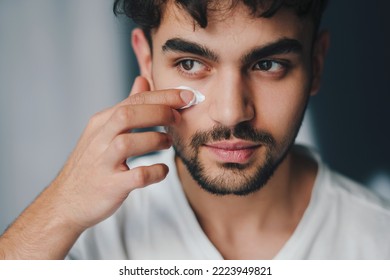 Close-up portrait of a man applying cream on face, indoors. Guy takes care of beauty and problem skin at home during covid-19 quarantine. Beauty skin. Skin care - Powered by Shutterstock