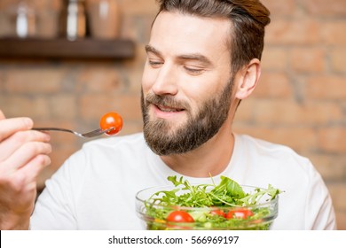 Close-up Portrait Of A Man Eating Salad With Tomatoes On The Red Brick Wall Background. Healthy And Vegan Food Concept