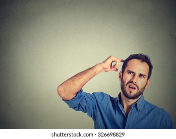Closeup portrait man scratching head, thinking deeply about something, looking up, isolated on grey wall background. Human facial expression, emotion, feeling, sign body language