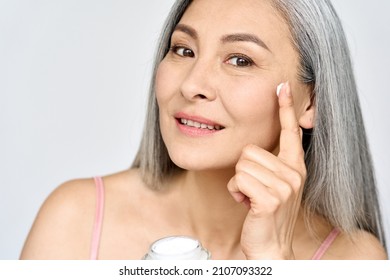 Closeup Portrait Of Mature Beautiful Middle Aged Asian Woman, Older Grey Haired Lady Looking At Camera Touching Face Applying Sunscreen Whitening Anti Age Perfect Skin Care Cream, Isolated On White.