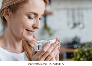 Closeup portrait of mature middle-aged woman warming up with coffee tea hot beverage cacao, drinking from a cup at home. Decaf coffee, feeling smell - Powered by Shutterstock