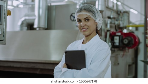 Closeup Portrait Of A Mature Woman Attractive Engineer Looking Straight Of The Camera And Smiling Large While Holding A Electronic Tablet In A Big Manufacturing Industry Factory