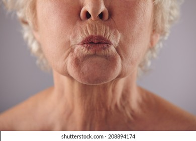 Close-up Portrait Of Mature Woman Puckering Lips Against Grey Background. 