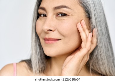 Closeup portrait of middle aged Asian woman's face with perfect skin. Older mature lady touching pampering face. Advertising of cosmetology salon plastic surgery procedures skincare.