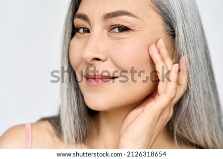 Closeup portrait of middle aged Asian woman's face with perfect skin. Older mature lady touching pampering face. Advertising of cosmetology salon plastic surgery procedures skincare.