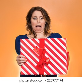 Closeup Portrait Middle Aged Woman Opening Gift Box Very Upset At What She Received, Isolated Orange Background. Negative Human Emotion, Facial Expression. Unsuccessful Holiday Shopping Concept