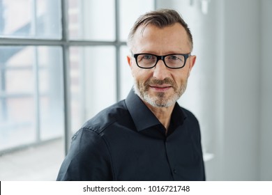 Close-up Portrait Of A Middle-aged Man Wearing Black Shirt And Eyeglasses While Looking At Camera With Confidence In The Office