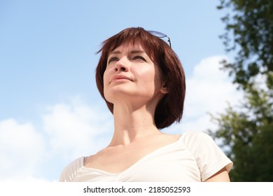 Close-up portrait of a middle-aged woman with brown hair against a blue sky. The woman looks into the distance with anxiety.