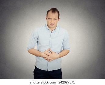 Closeup Portrait Miserable Upset Young Man, Doubling Over In Acute Body Stomach Pain, Looking Very Sick Isolated Grey Wall Background. Negative Facial Expression Emotion Feeling Health Issues Concept 