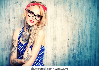 Close-up portrait of a modern pin-up girl wearing old-fashioned polka-dot dress and spectacles and modern dreadlocks. Fashion shot. Tattoo.