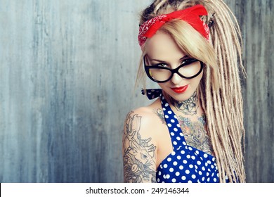Close-up portrait of a modern pin-up girl wearing old-fashioned polka-dot dress and spectacles and modern dreadlocks. Fashion shot. Tattoo.