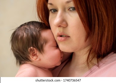 Closeup Portrait Of Mother With Serious Face Embracing Newborn Baby Daughter. Young Mom Holding In Arms Little Infant Child With Closed Eyes. Mother And Child Bonding And Maternity Issues Concept