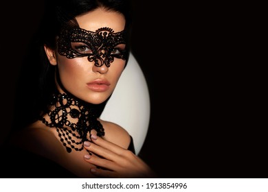 Close-up portrait mysterious attractive woman. Black background, with lace mask on face, leather dress. Beauty passionate girl, hand near face. The concept of the Halloween party and parade