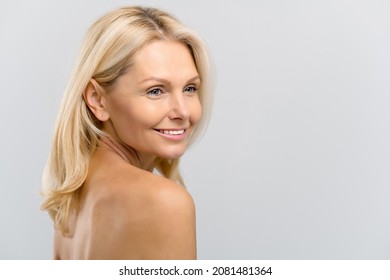 Close-up Portrait Of Naked Middle-aged Lady Looking Aside And Smiling Dreamy. Well-looking Serene Mature Blonde Woman With Smooth Pure Skin Over Grey Background