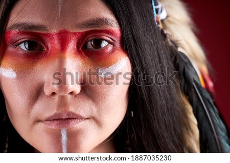 close-up portrait in native american style, beautiful woman in Indian hat and drawings on face, trendy color photo. accessories Bohemians and Boho