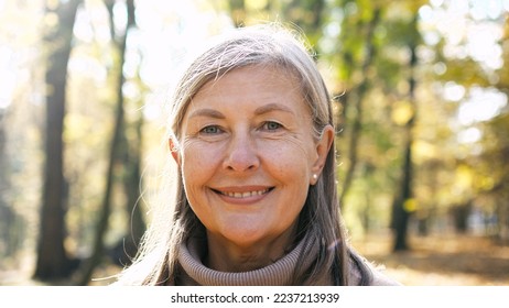 Close-up portrait of naturally beautiful senior cute gray-haired woman standing in park in autumn wearing coat looking at camera smiling. Pretty mature kind good-looking female on fresh air. - Shutterstock ID 2237213939